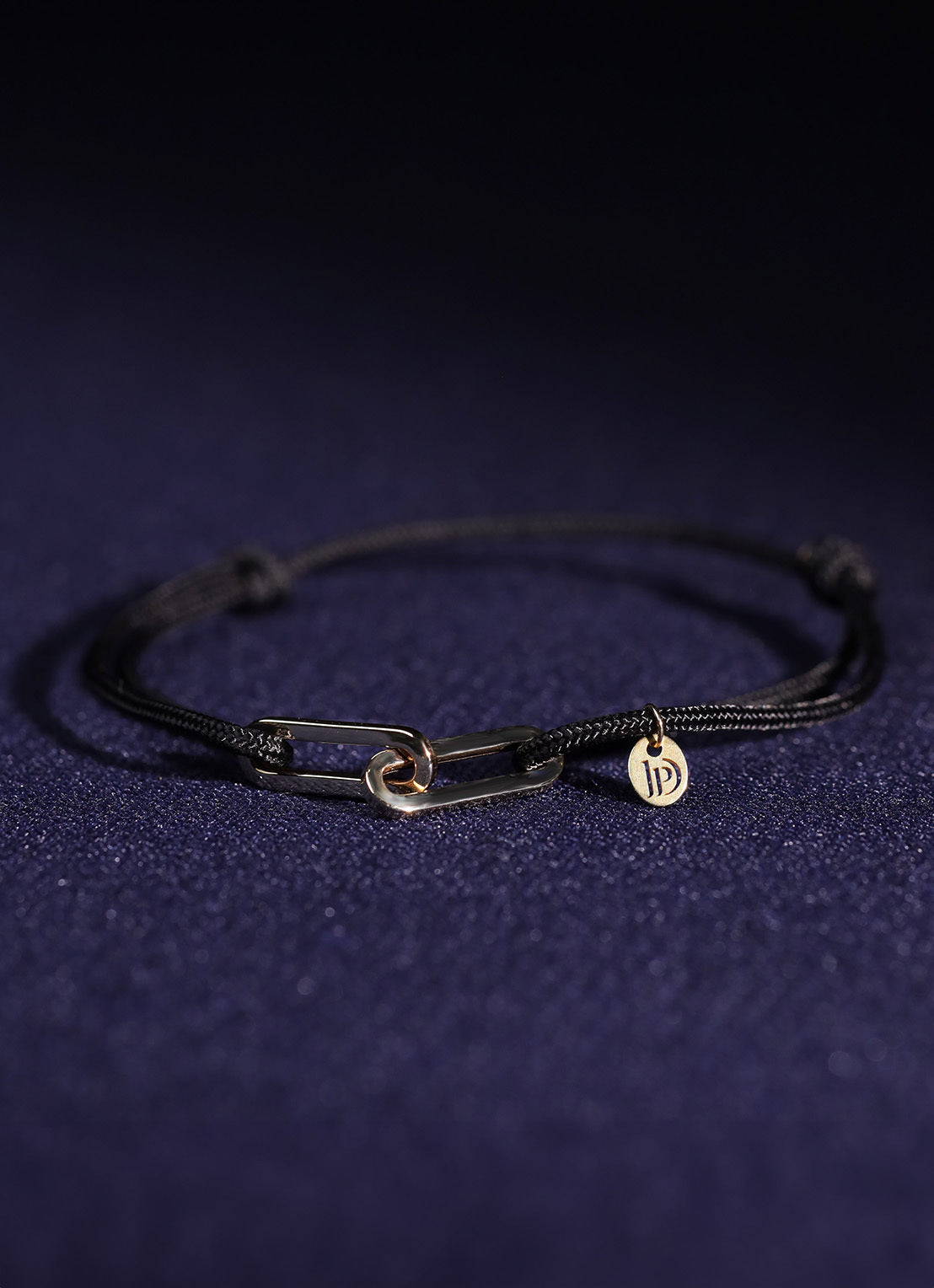 Black cord bracelet with yellow-gold-tone link closure and round charm