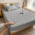 Quilted padded mattress topper with square stitch design on a bed