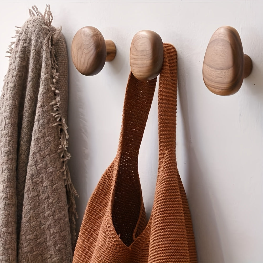 Pebble-shaped wooden decorative wall hooks mounted on a white wall
