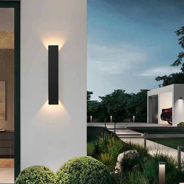 Black vertical outdoor LED wall light casting warm white light upward and downward