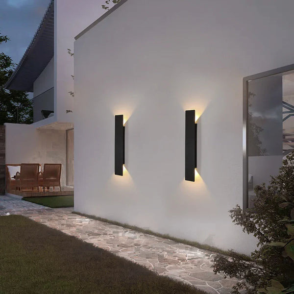 Black vertical outdoor LED wall light casting warm white light upward and downward