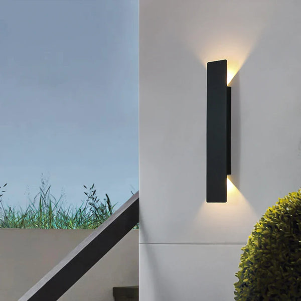 Black vertical outdoor LED wall light casting warm white light upward and downward