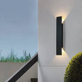 Black vertical outdoor LED wall light casting warm white light upward and downward