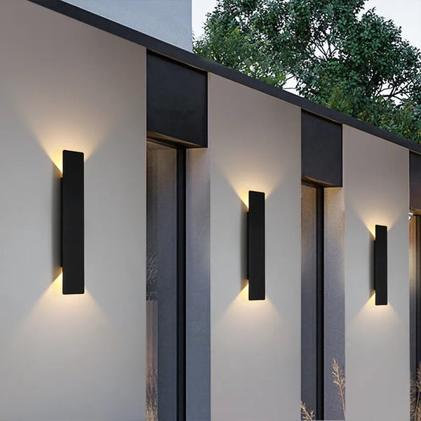 Black vertical outdoor LED wall light casting warm white light upward and downward