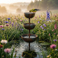 Three-tier rustic brown bird bath with stacked bowls in a garden
